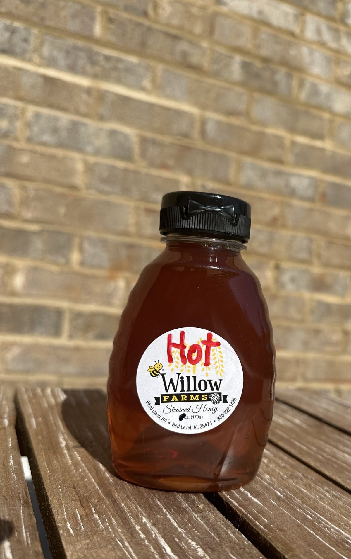 Willow Farms Hot Honey squeeze bottle on a wooden bench